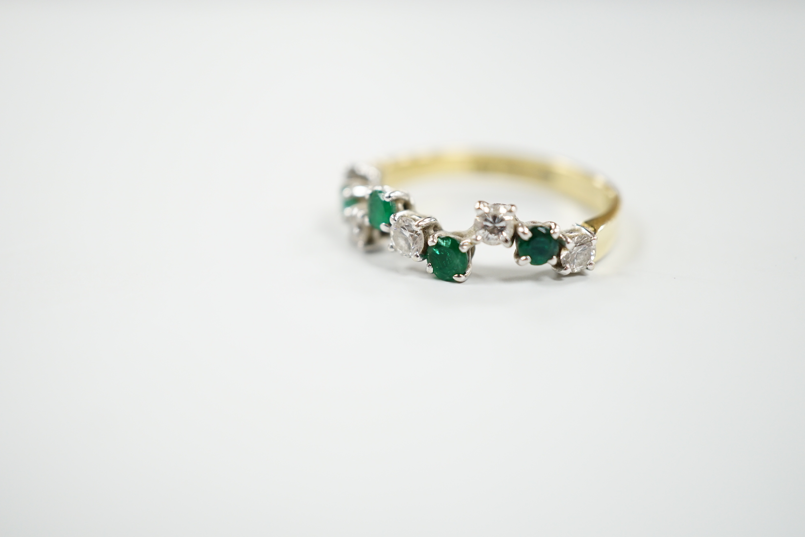 A modern 18ct gold, four stone emerald and five stone diamond set wavy half hoop ring, size O, gross weight 2.8 grams.